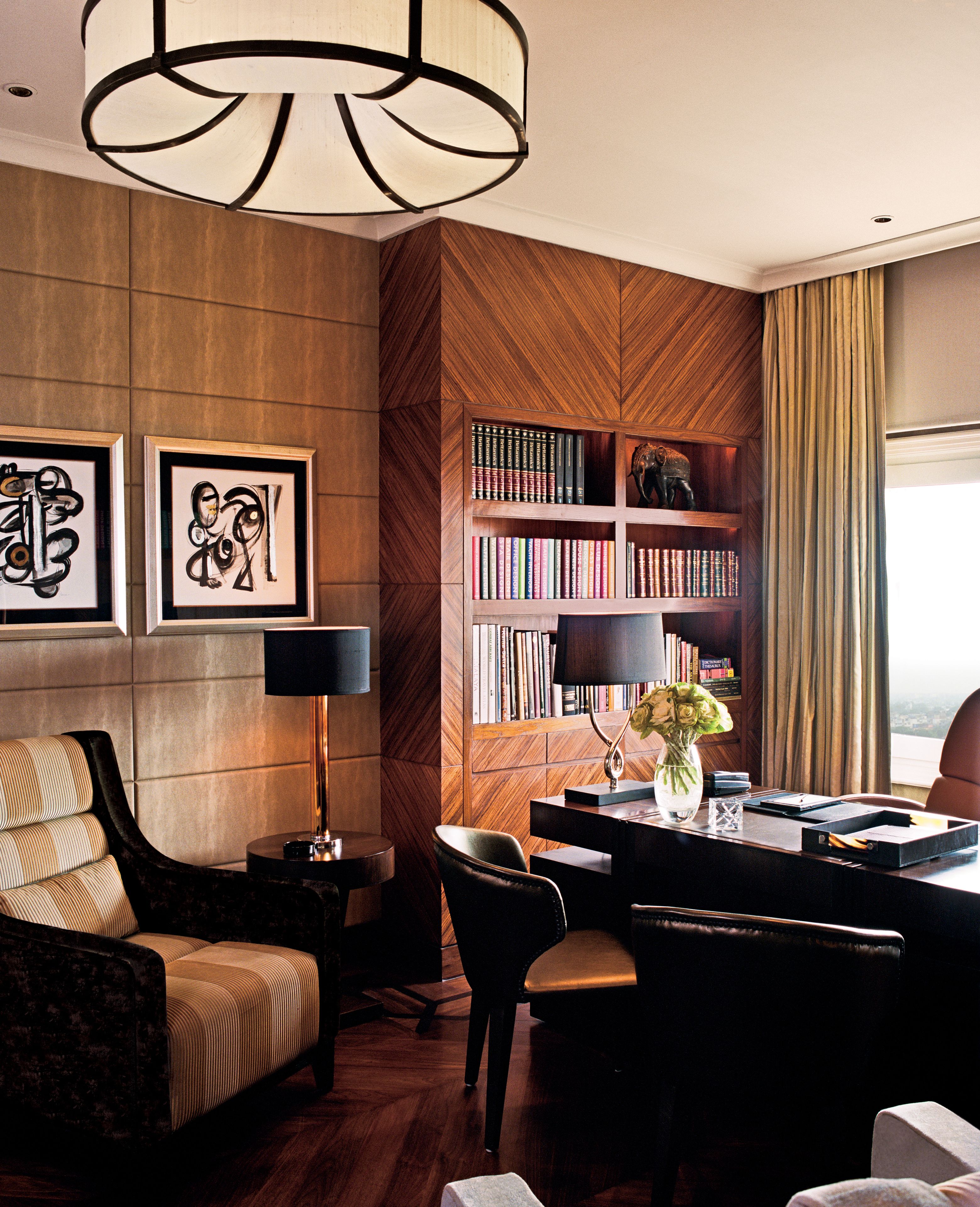 A modern hotel room with a wooden accent wall, a bookshelf, a dining area with a table and chairs, and a large window with curtains.
