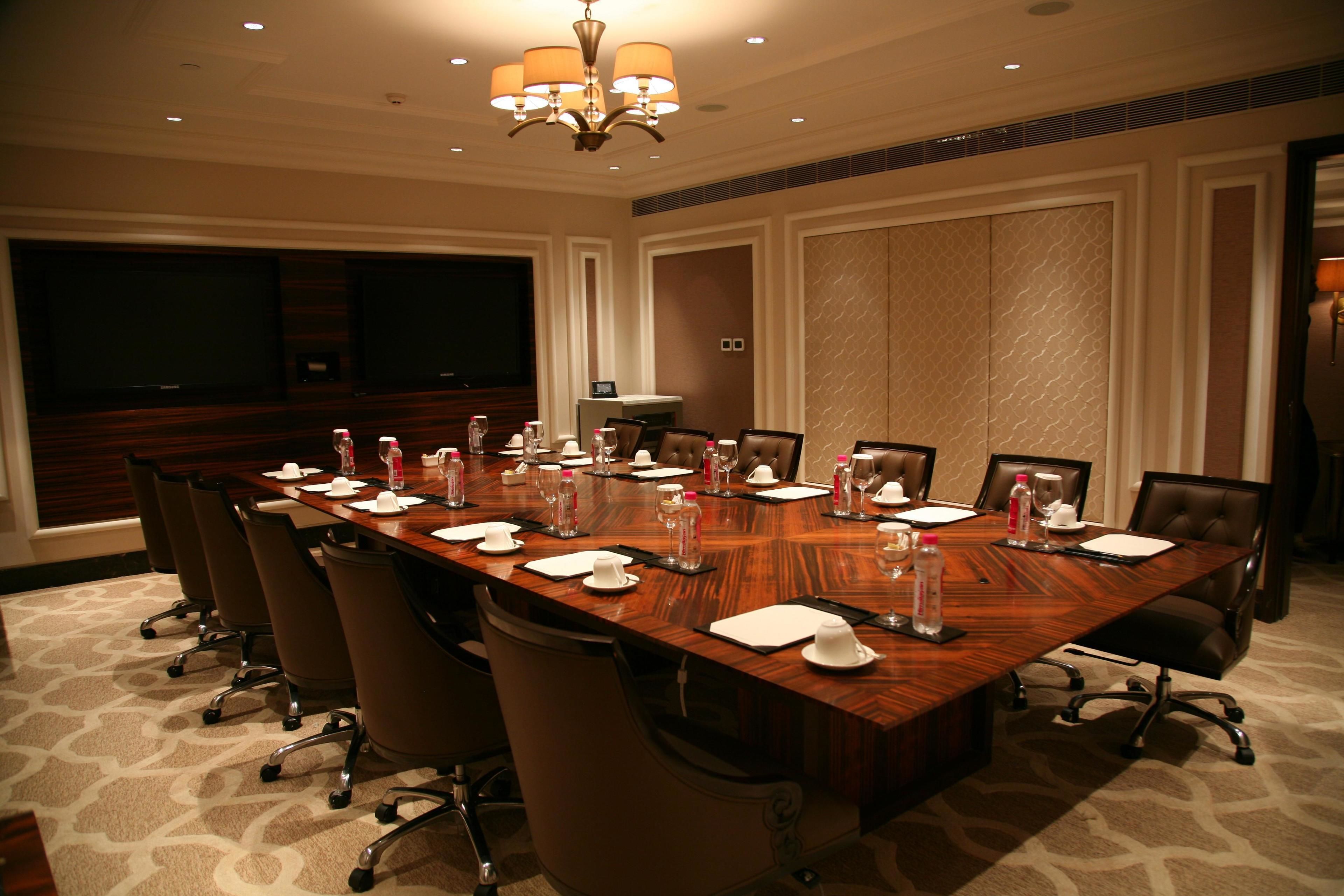 A conference room with a long table, chairs, a projector screen, and a chandelier.