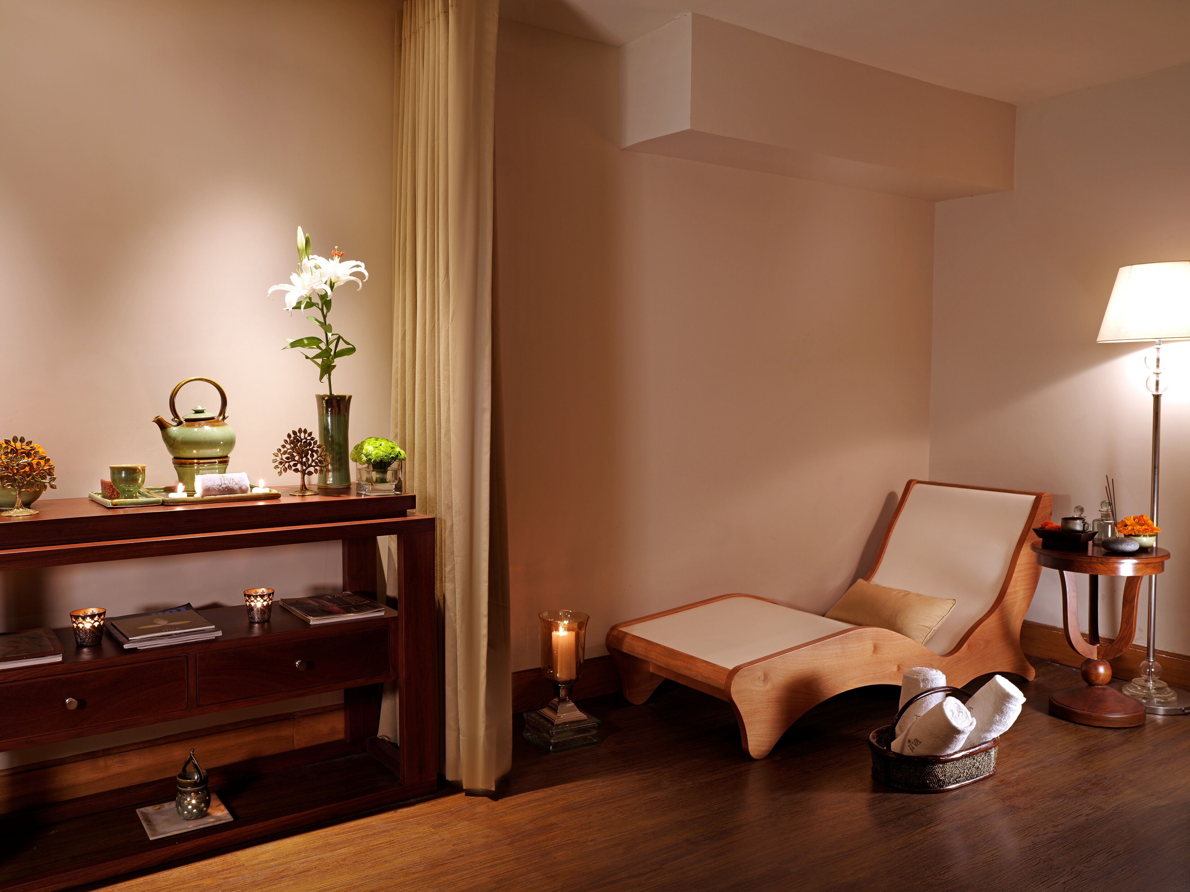 A room with a wooden desk, a cushioned chair, a floor lamp, and a small table with a candle.
