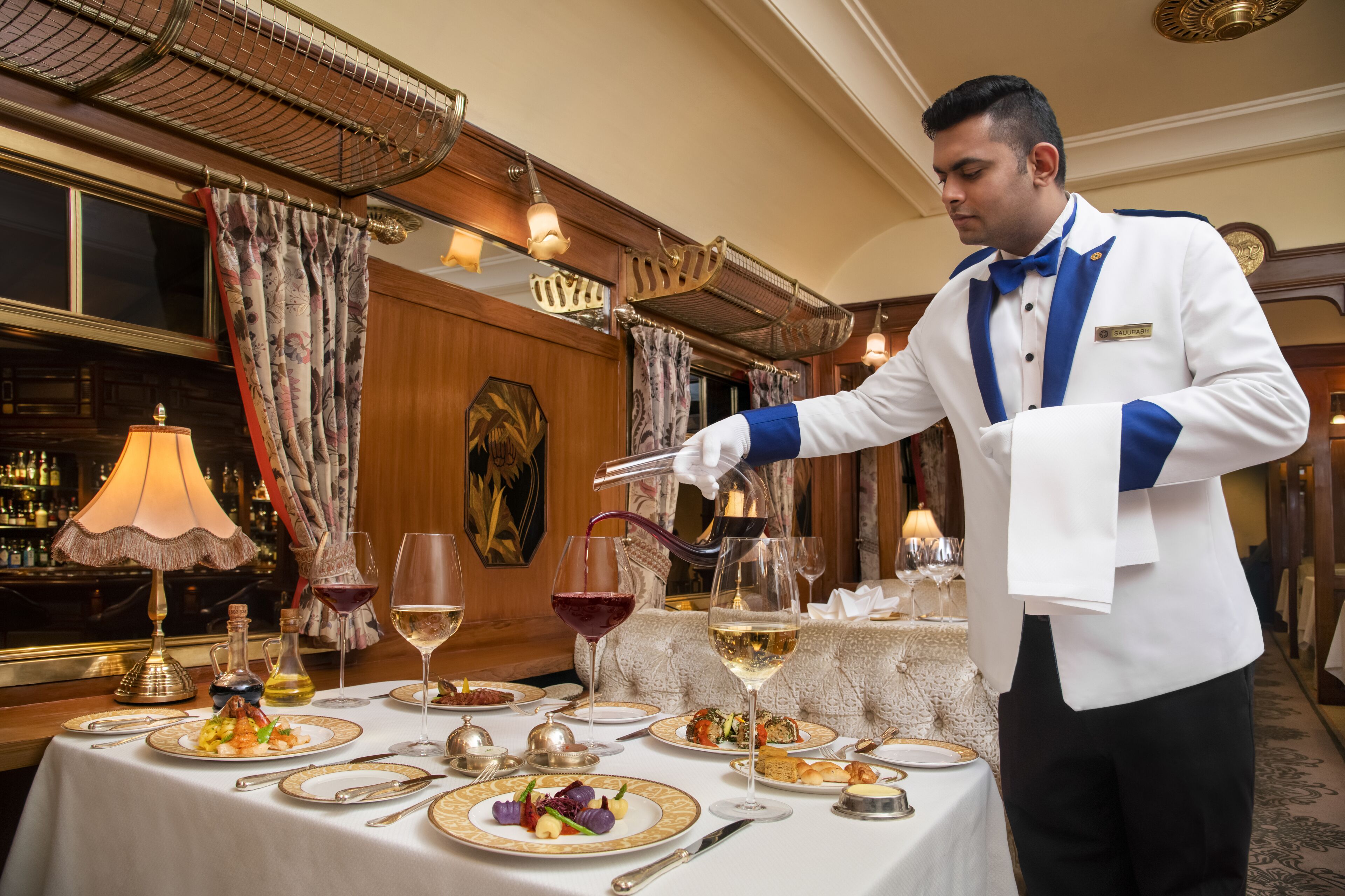 A waiter serving a meal in a well-decorated dining area with a bar and elegant furnishings.