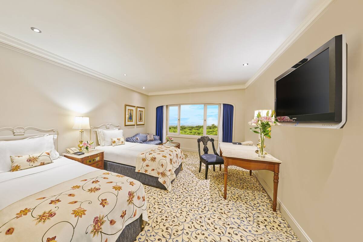 A hotel room with two beds, a desk, a chair, a TV, and a large window with a view.