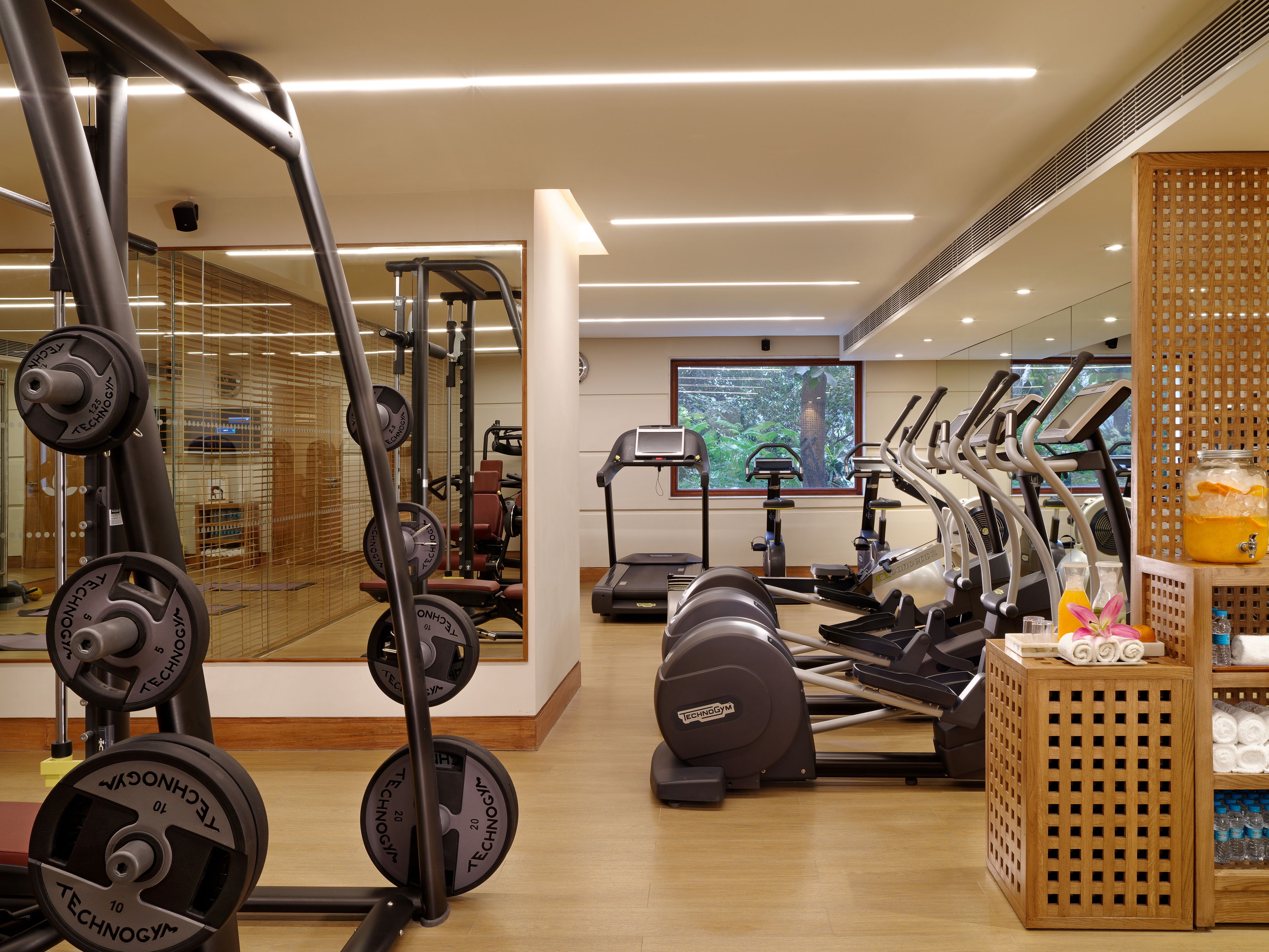A gym with various exercise equipment, including treadmills and weight machines, and a large window with a view of greenery.
