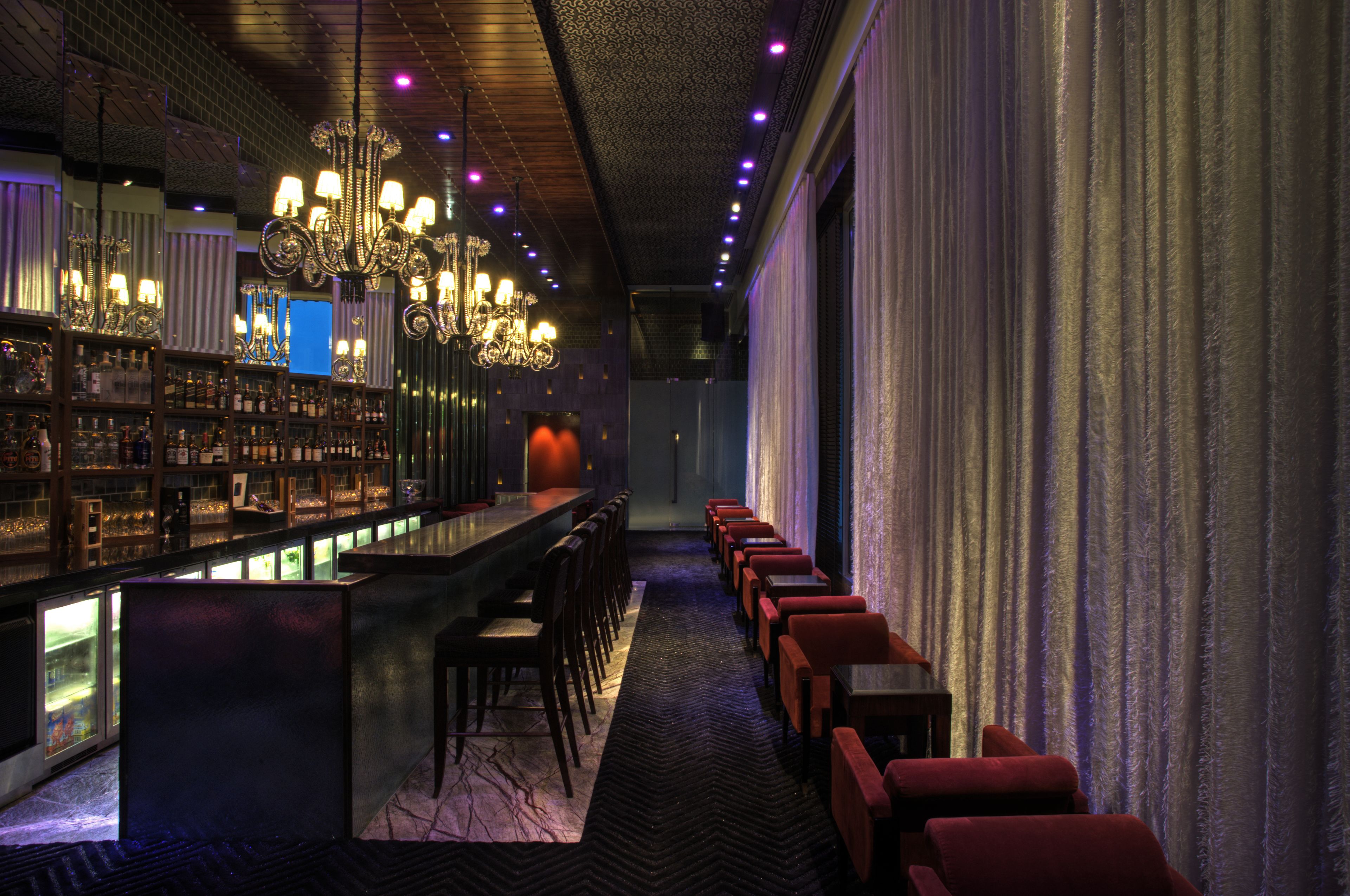 A bar area with a long counter, multiple chairs, and a chandelier.