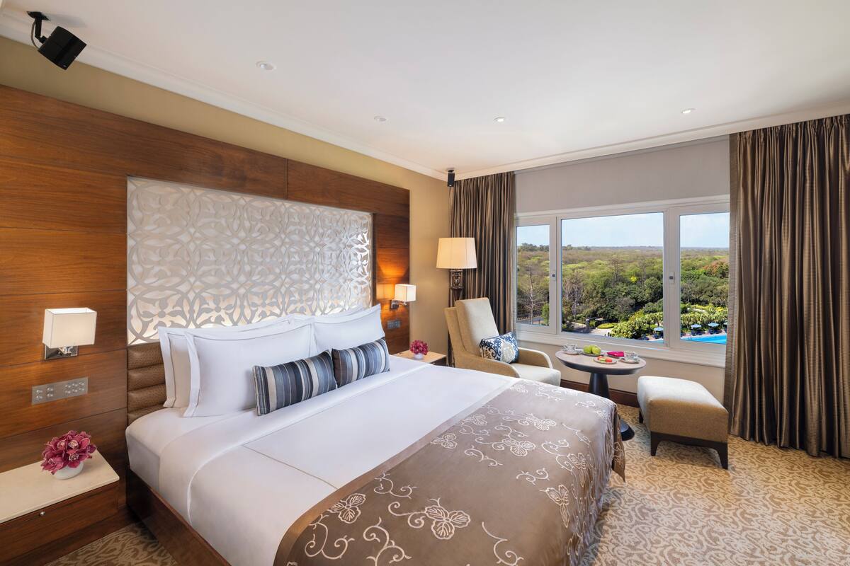 A hotel room with a large bed, a sitting area with a chair and table, and a view of the outdoors.