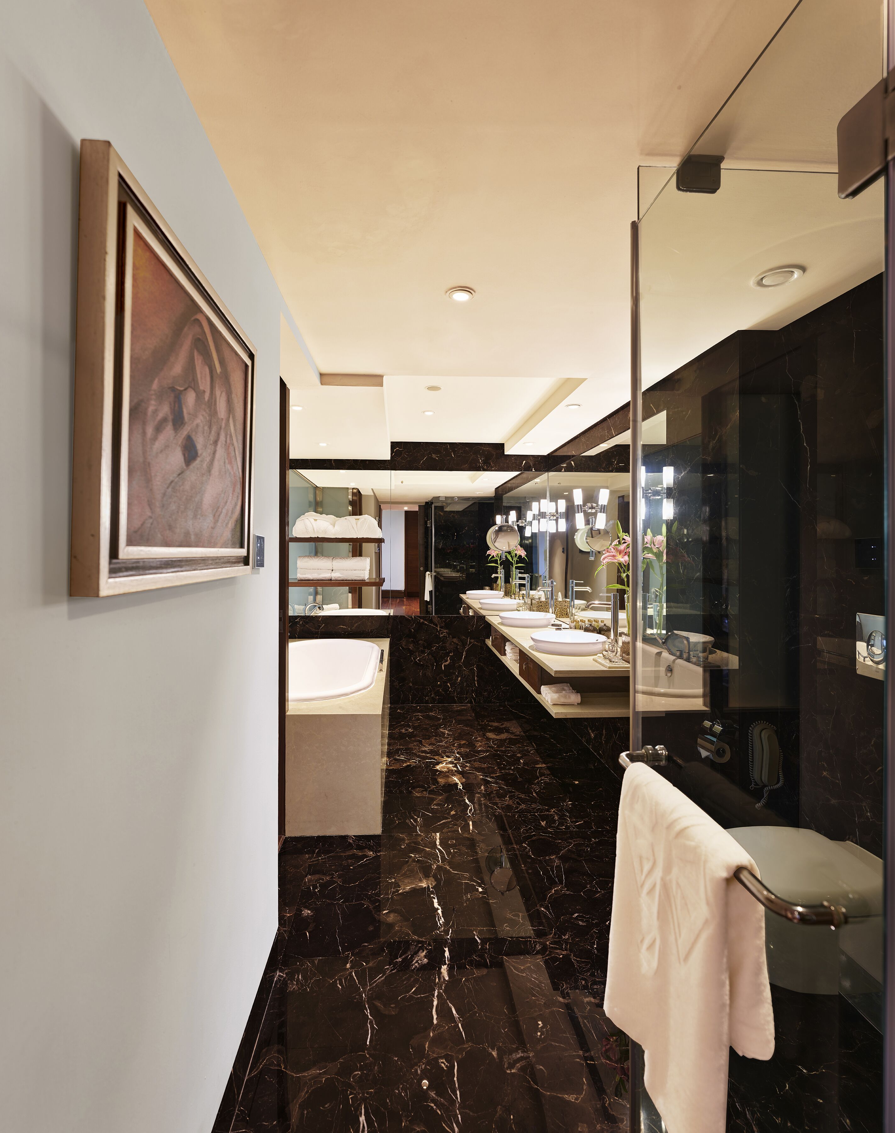 A modern bathroom with a marble floor, dual sinks, a large mirror, and a framed artwork on the wall.