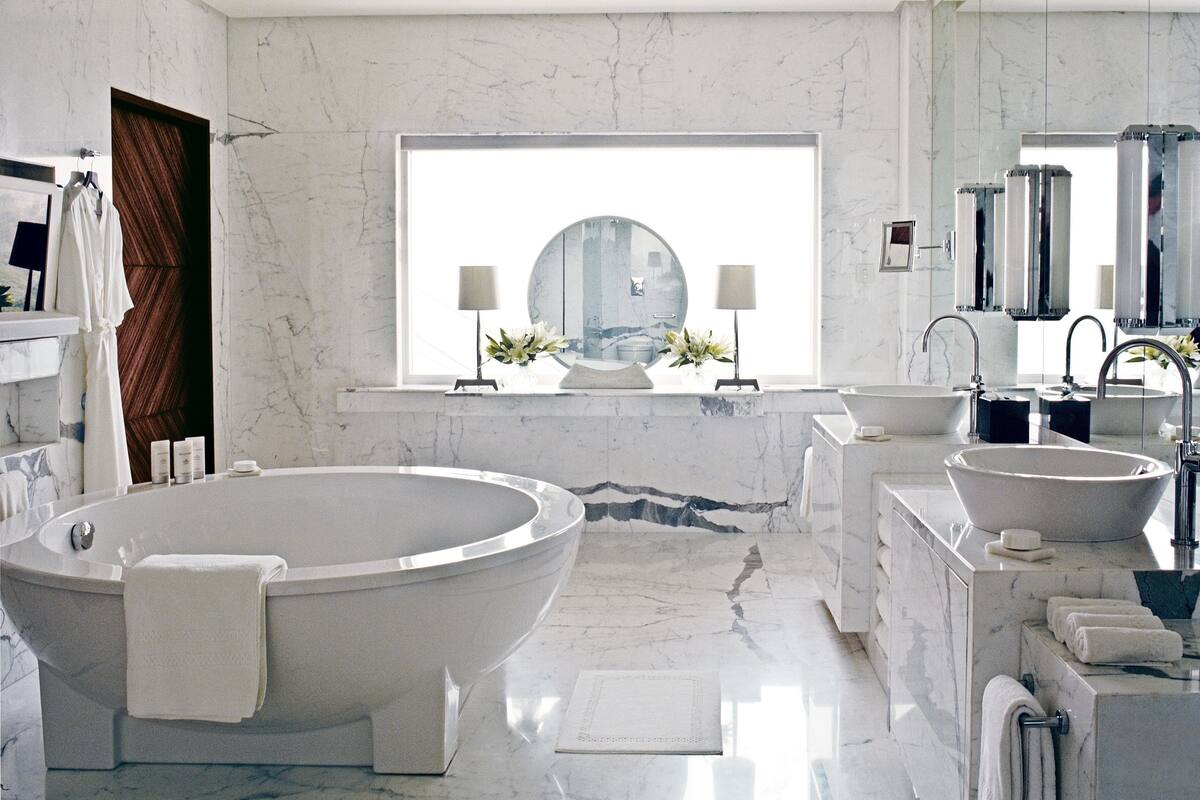 A modern bathroom with a freestanding bathtub, two sinks, a large mirror, and a window with a view.