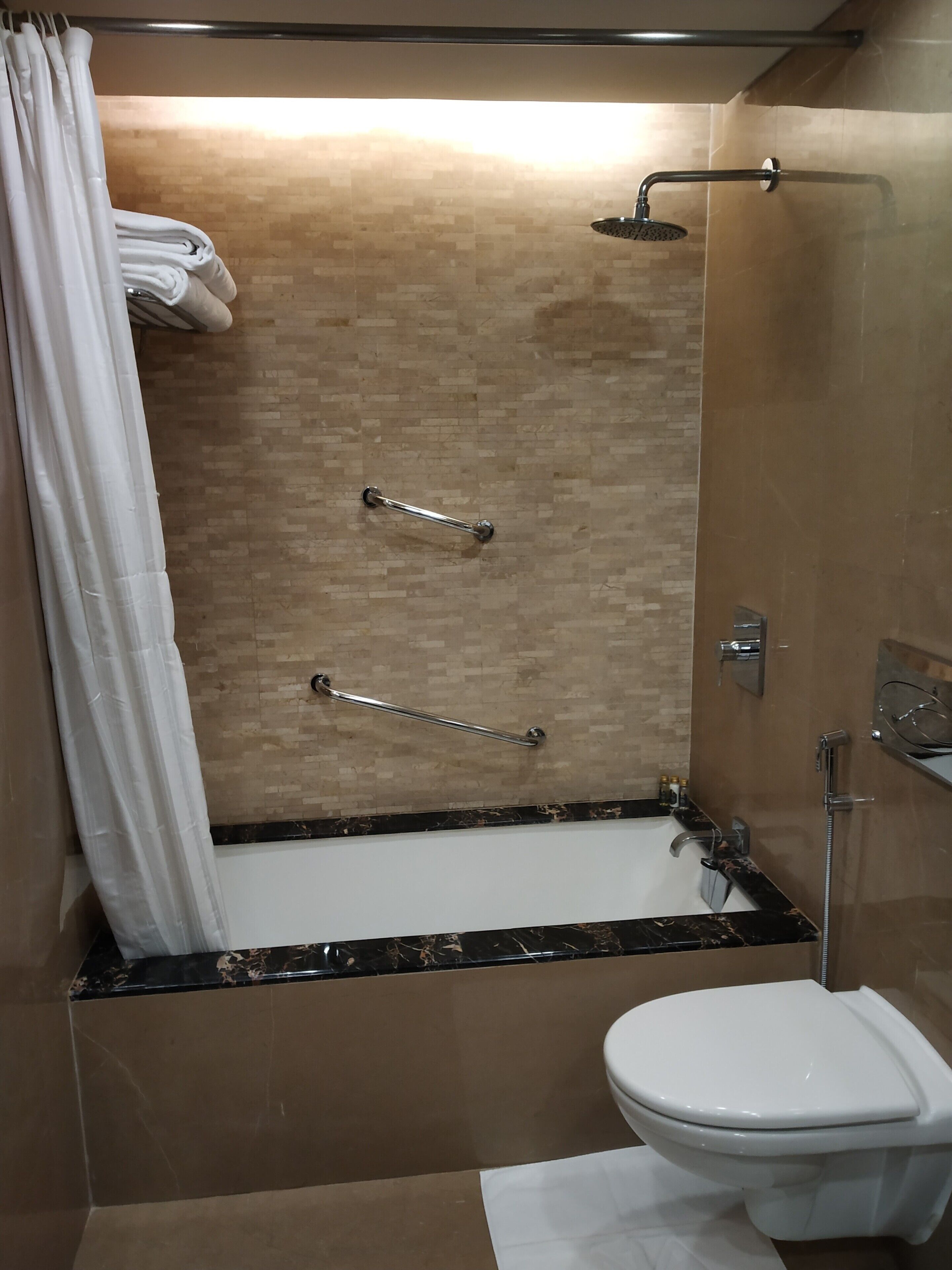 A bathroom with a shower, grab bars, a toilet, and a towel rack.