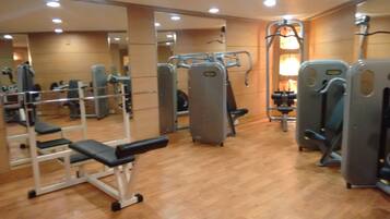 A gym with various exercise machines, mirrors, and wooden flooring.