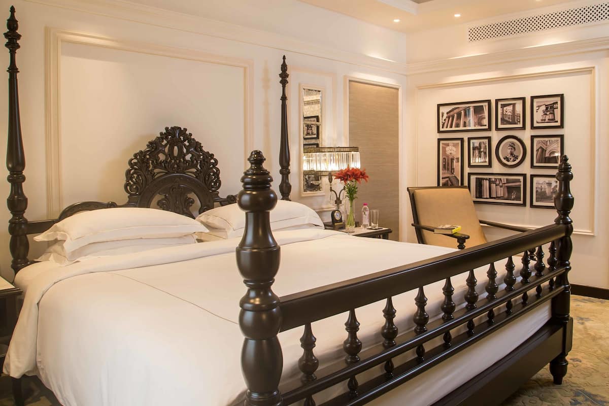 A neatly made bed with a dark wooden headboard and footboard, a nightstand with a lamp, and a chair with a small table beside the bed.