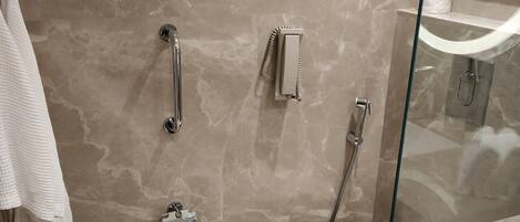 Un baño con pared de mármol, inodoro, cabina de ducha de vidrio y un perchero para toallas.