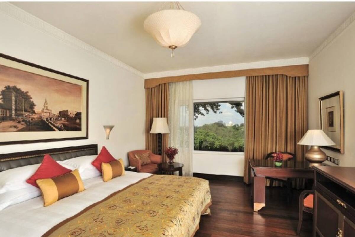 A hotel room with a large bed, a desk, a chair, a lamp, and a window with curtains.