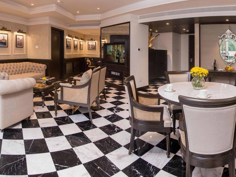 A hotel lobby with a checkered floor, a sofa, a dining area with a round table and chairs, and framed pictures on the walls.