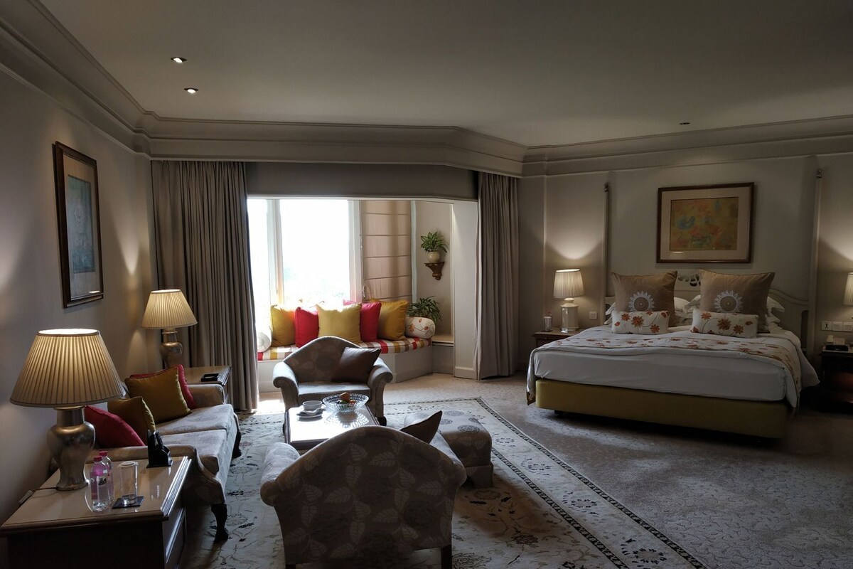 A hotel room with a bed, a sofa, a chair, a desk, and a window with curtains.