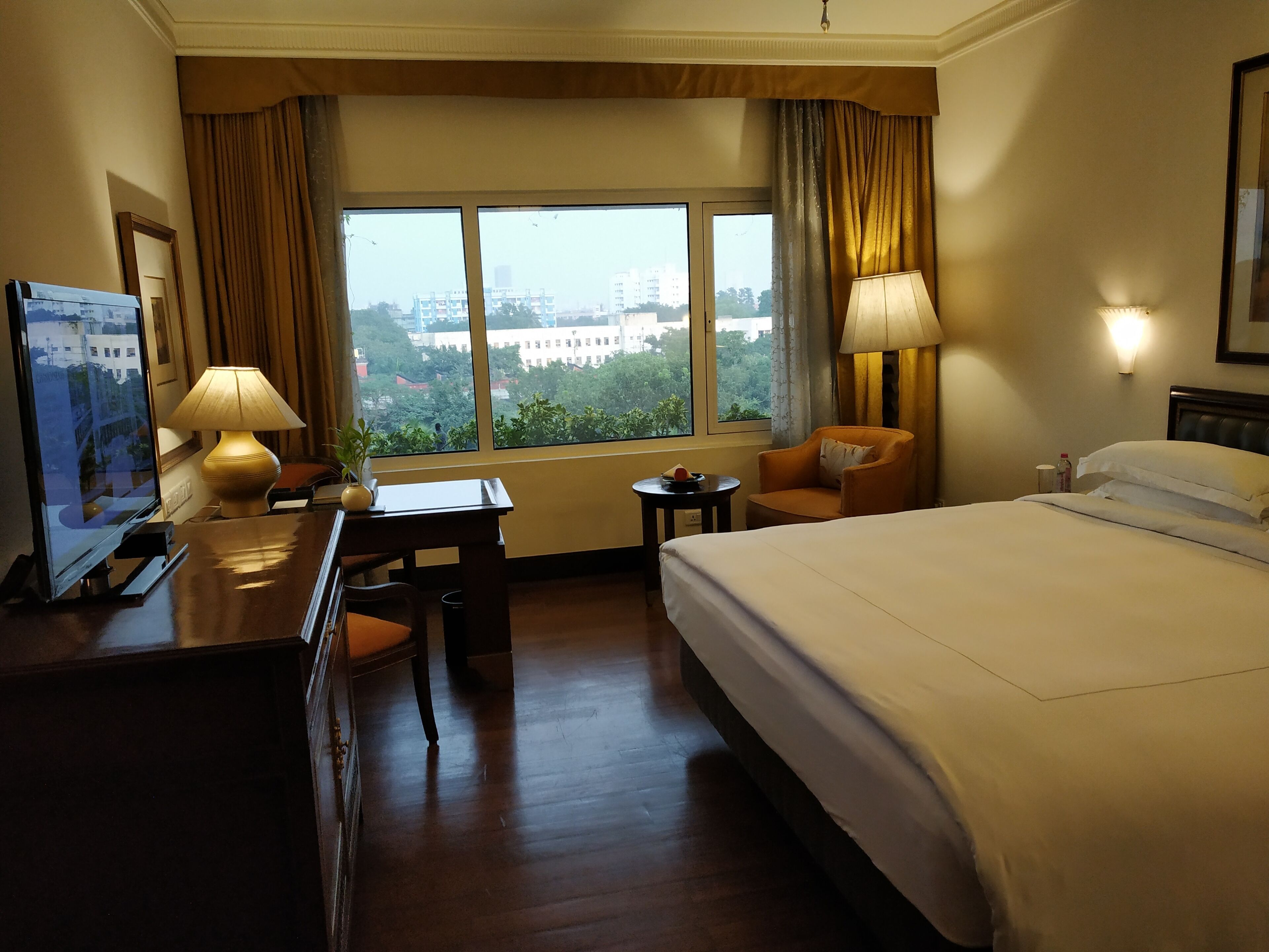 Una habitación de hotel con una cama grande, un escritorio con lámpara, una silla y una televisión.