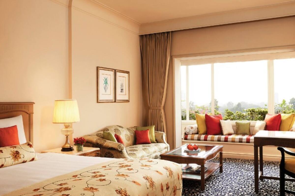 A hotel room with a bed, a sofa, a desk, and a large window with a view of greenery.