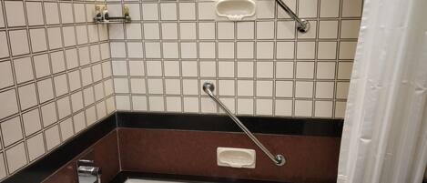 A bathroom with white tiled walls, a black and brown lower section, a white bathtub, and a shower area with a grab bar.