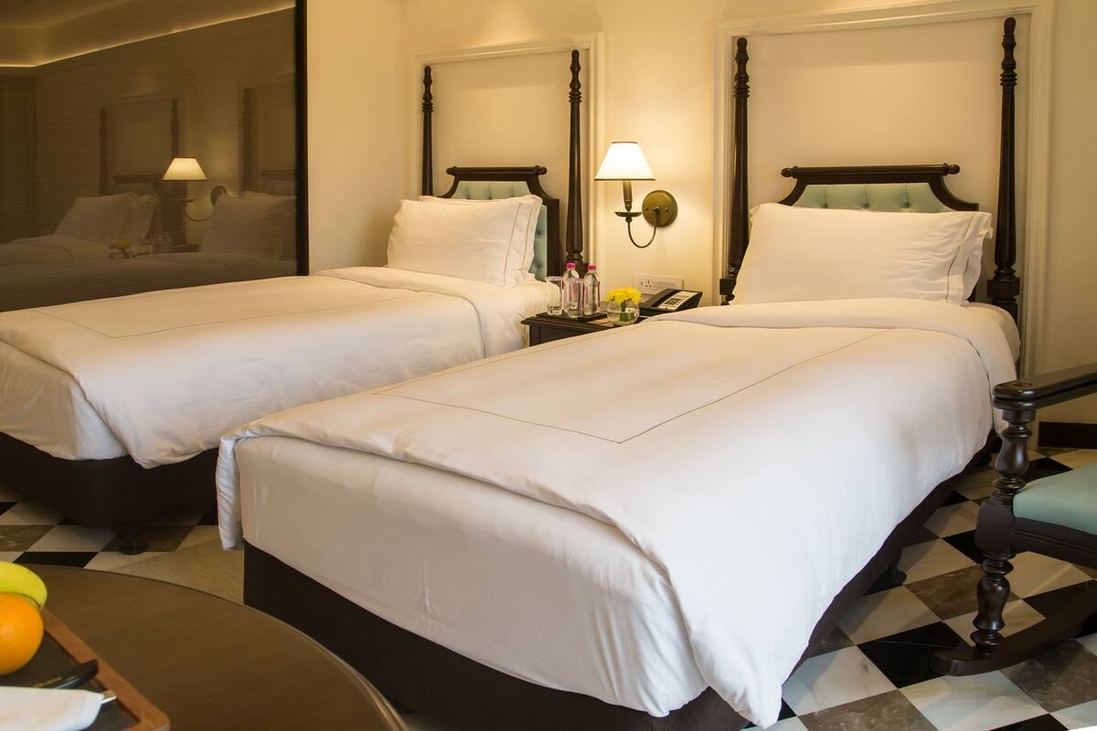 A hotel room with two single beds, a small table with fruit, and a checkered floor.