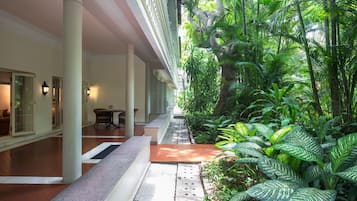 A hotel corridor with a central walkway surrounded by lush greenery and a seating area with a table and chairs.
