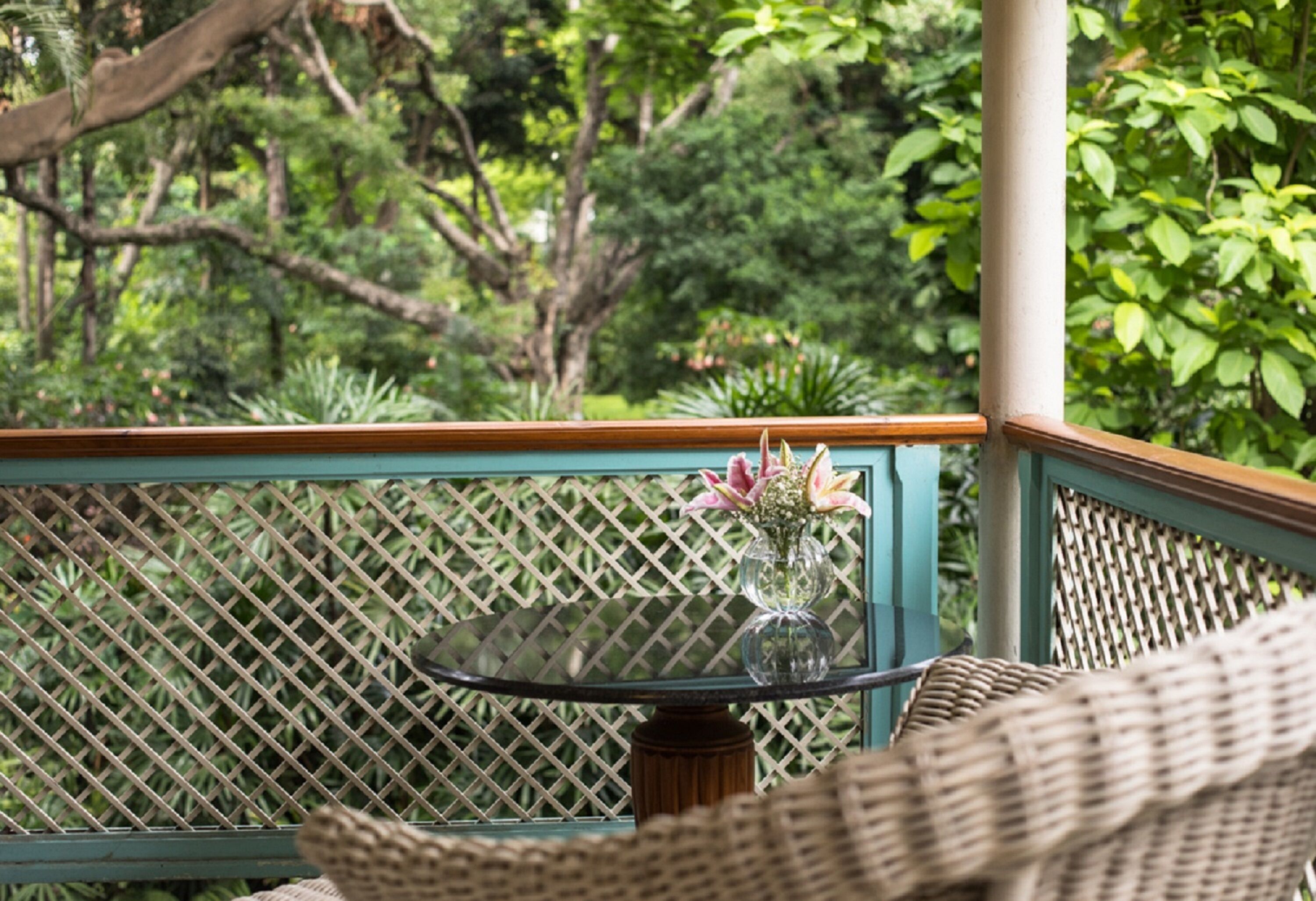 A glass table with a vase of flowers on a balcony with a lattice railing.