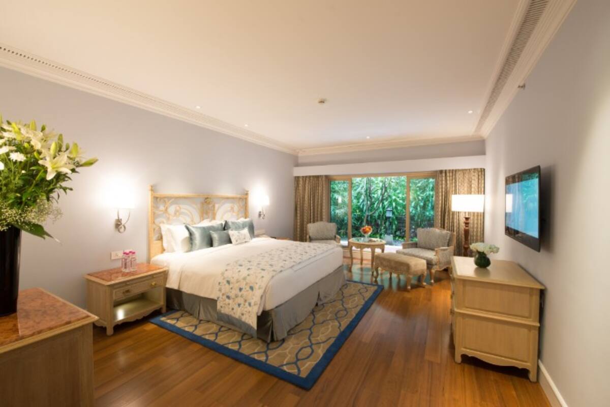 A hotel bedroom with a large bed, bedside tables, a TV, and a view of greenery through the window.