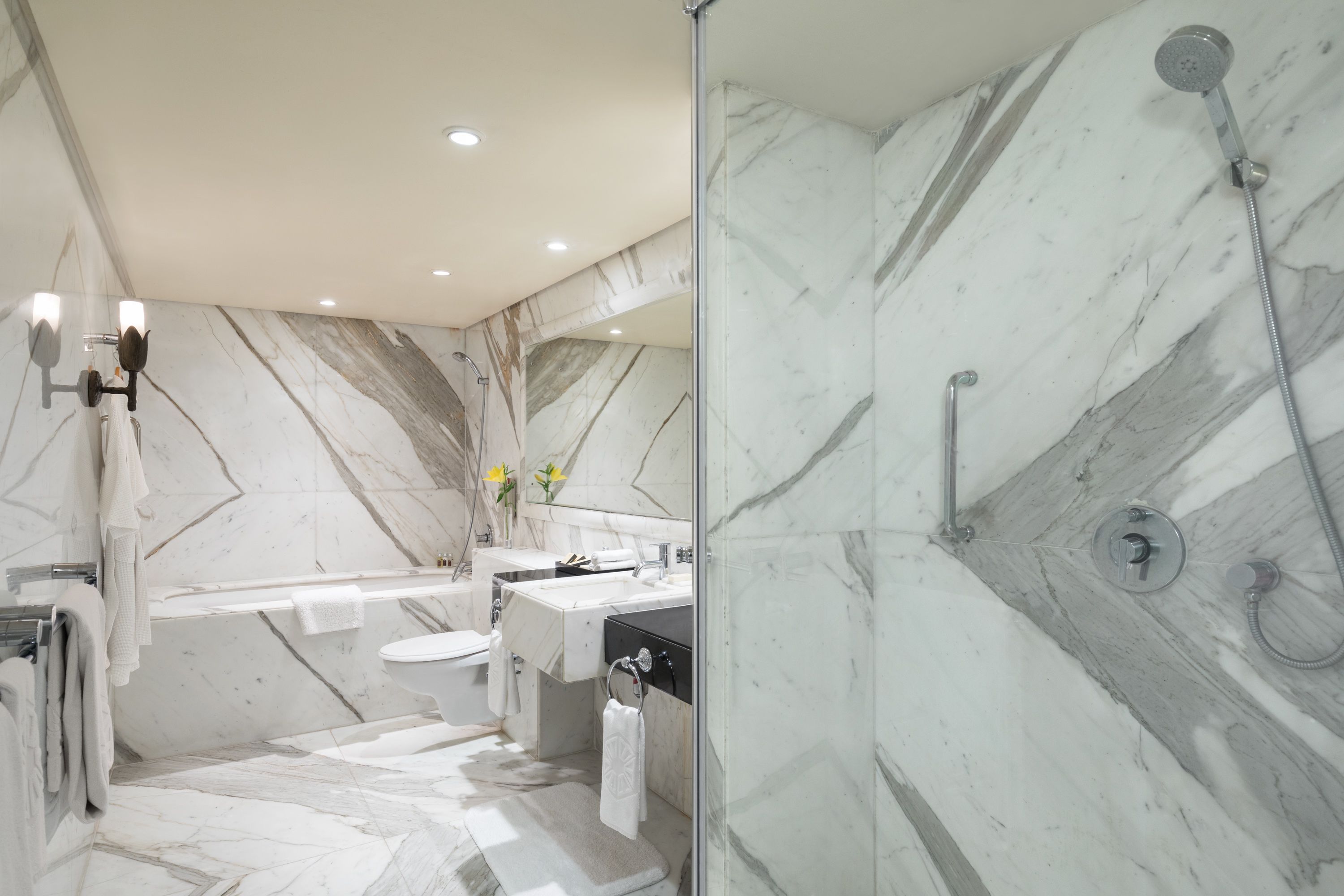 A modern bathroom with a marble floor, a glass-enclosed shower, a bathtub, and a vanity with a mirror.