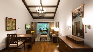 A spacious living area with a wooden floor, a chandelier, a dining table with chairs, a sofa, a coffee table, and a large mirror.