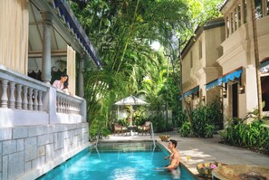 Un área de piscina con superficie de agua cristalina, rodeada de exuberante vegetación y elementos arquitectónicos.