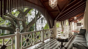 A covered outdoor area with a checkered floor, a white railing, and a large tree in the background. - Taj West End (Bengaluru)