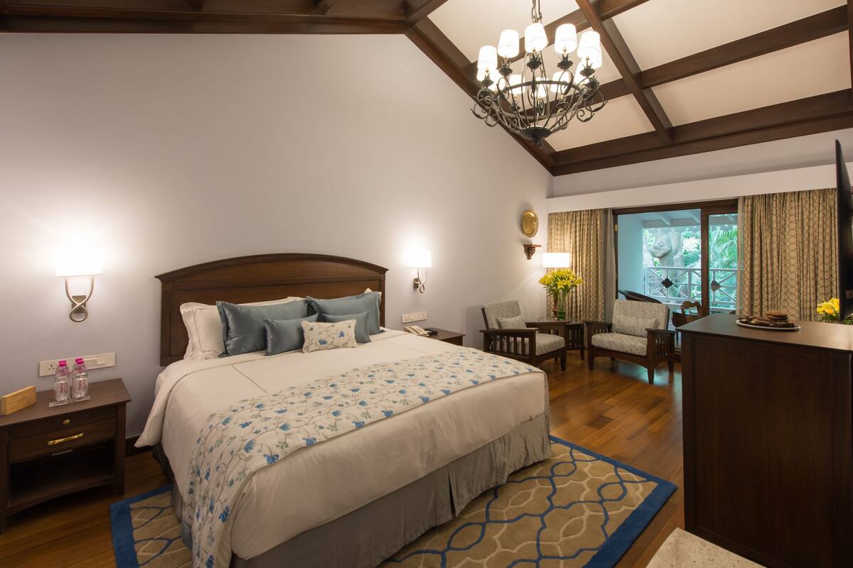 A bedroom with a large bed, a chandelier, a desk, and a view of the outdoors.