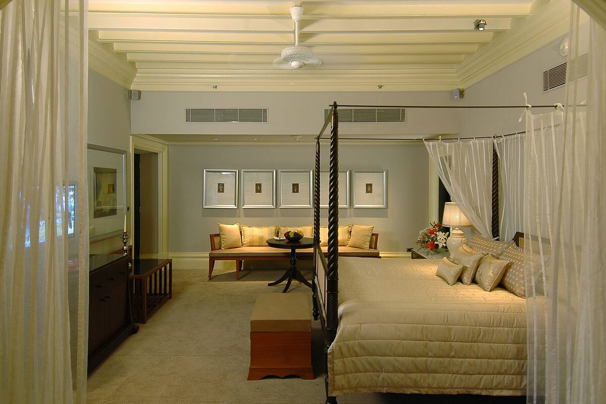 A bedroom with a four-poster bed, a sofa, a dining table, and a chandelier.