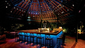 An indoor bar area with a high ceiling and wooden beams, featuring a bar counter with stools and a small seating area. - Taj West End (Bengaluru)