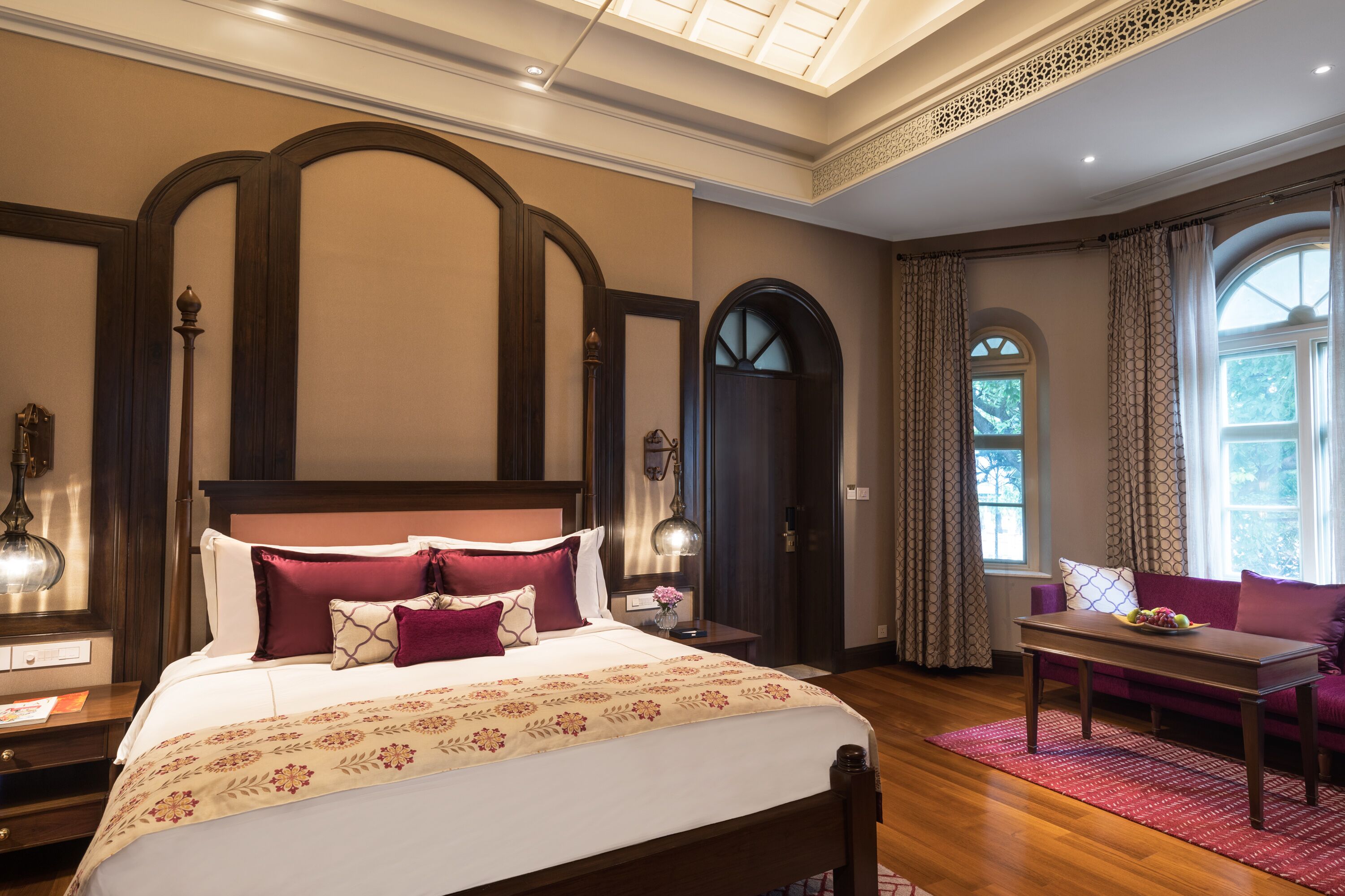 A hotel room with a large bed, a wooden headboard, a nightstand, a table, and a window with curtains.