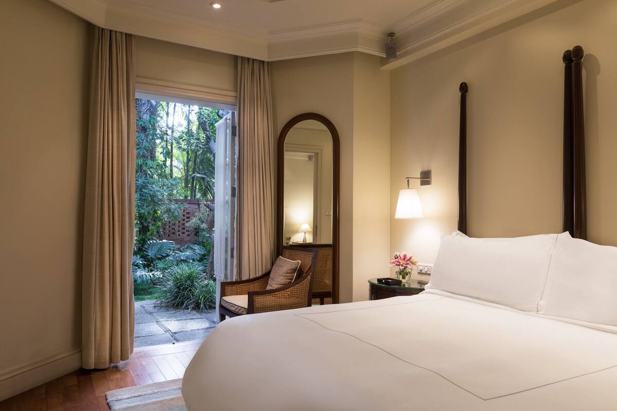 A hotel room with a large bed, a chair, a nightstand with a lamp, a mirror, and a view of the outdoors.
