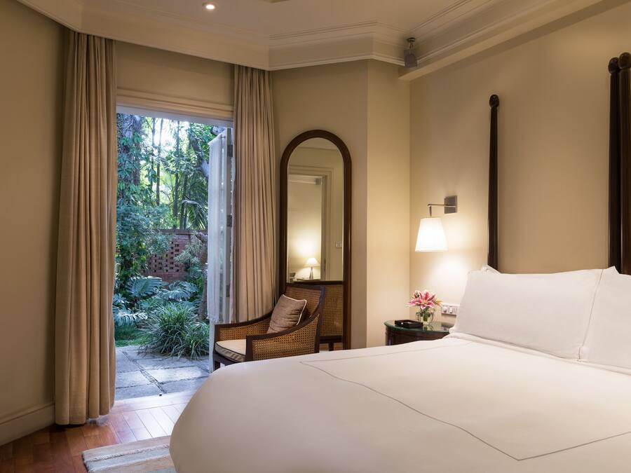 Ein Hotelzimmer mit einem großen Bett, einem Sessel, einem Nachttisch mit Lampe, einem Spiegel und Blick ins Freie.