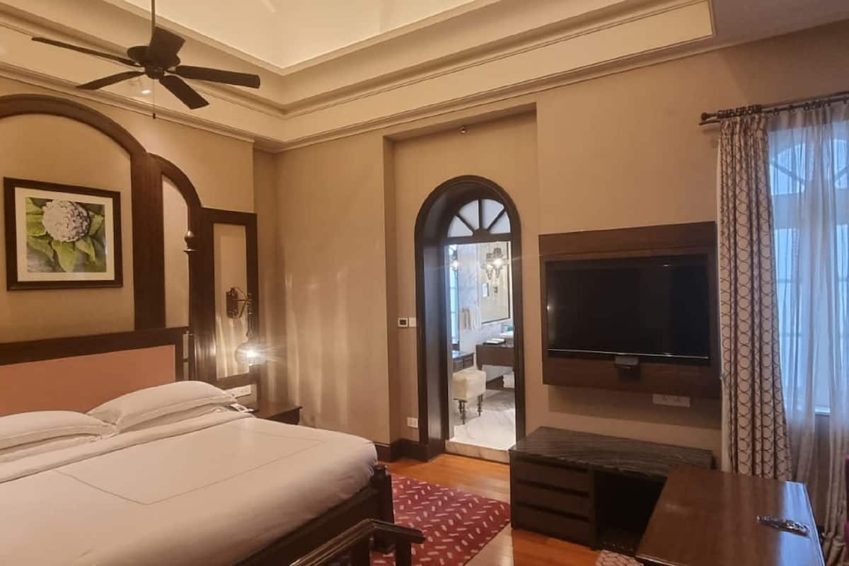 A hotel room with a large bed, a TV, a ceiling fan, and a view of the adjacent room.