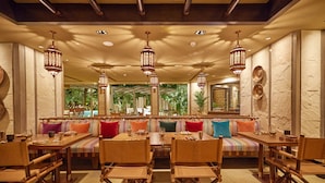 A restaurant with high tables and benches, ornate hanging lanterns, and a view of greenery outside. - Taj West End (Bengaluru)