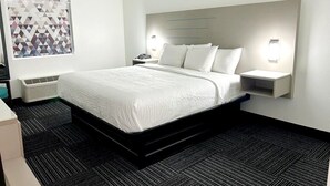 A modern hotel room with a large bed, bedside tables, a wall-mounted light, and a geometric artwork on the wall. - Baymont by Wyndham Port Wentworth (Port Wentworth)