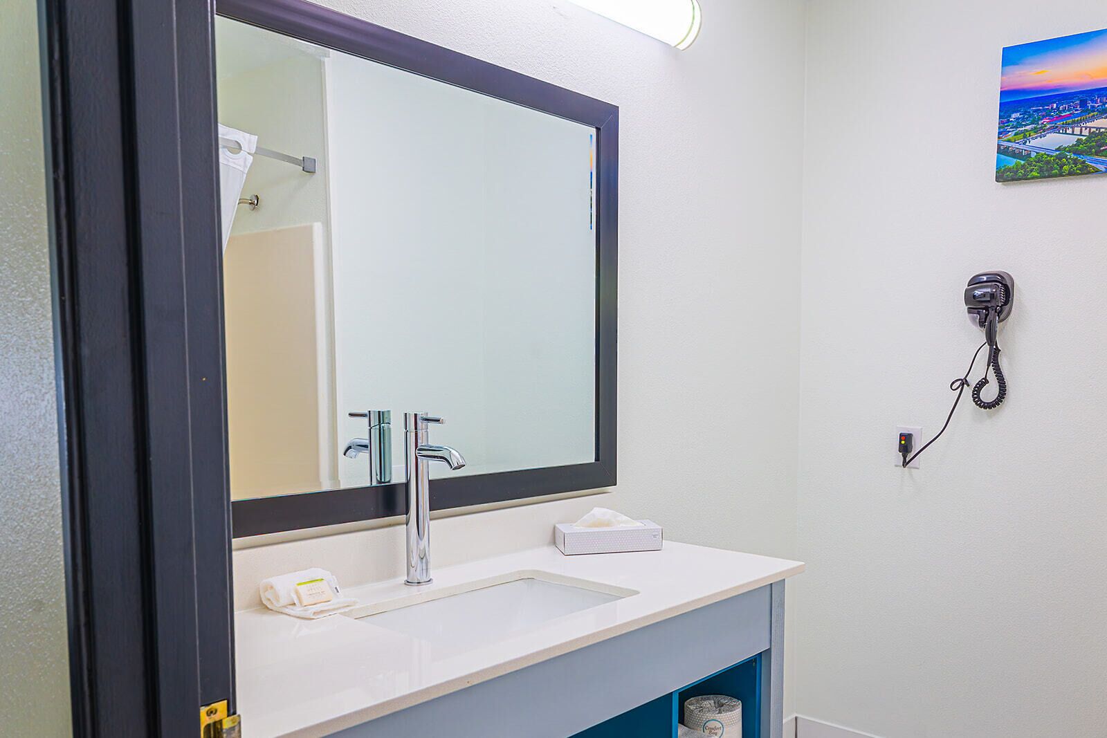 A bathroom with a large mirror, a sink, a towel rack, a tissue box, and a phone mounted on the wall.
