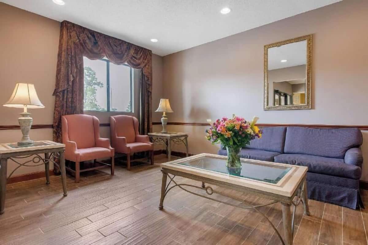 A hotel room with a sofa, two armchairs, a coffee table, a mirror, and a window with curtains.
