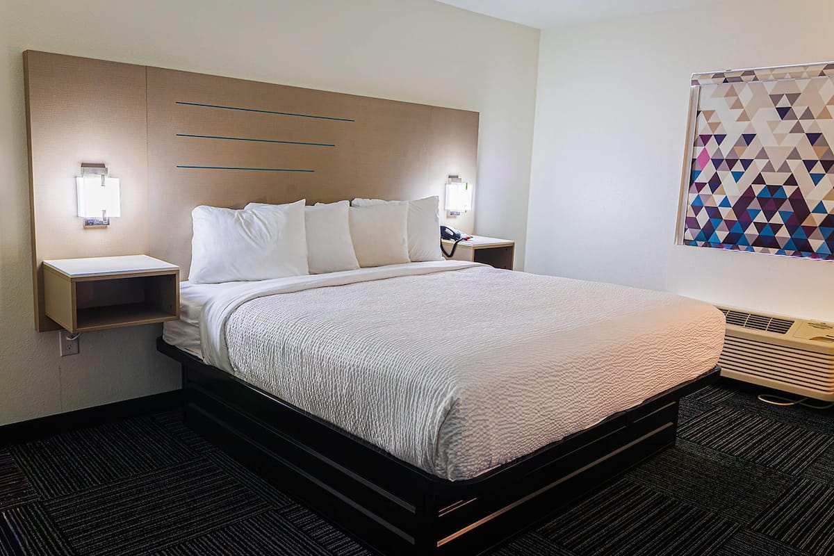 A hotel room with a large bed, bedside tables, a wall-mounted air conditioner, and a geometric-patterned curtain.
