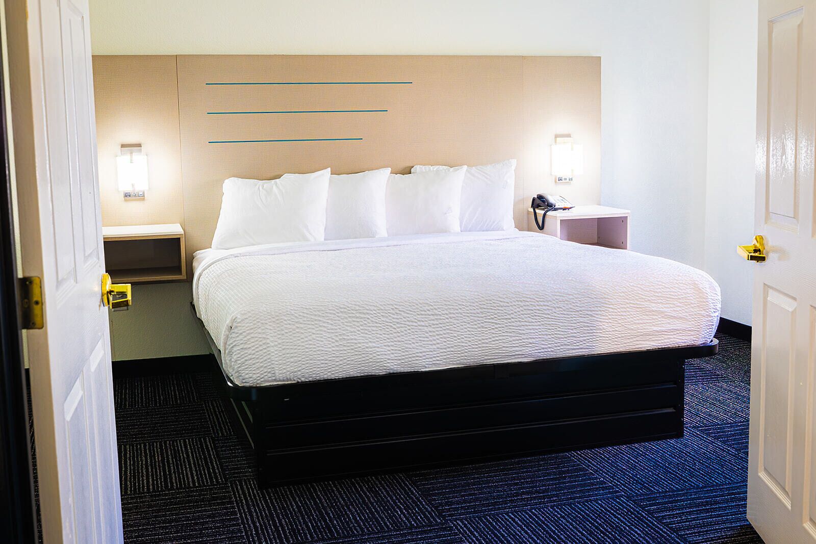 Una habitación de hotel con cama, mesitas de noche y luces empotradas en la pared.
