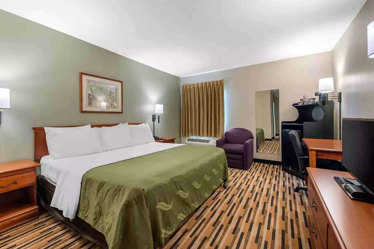 A hotel room with a bed, a desk, a chair, a television, and a mirror.