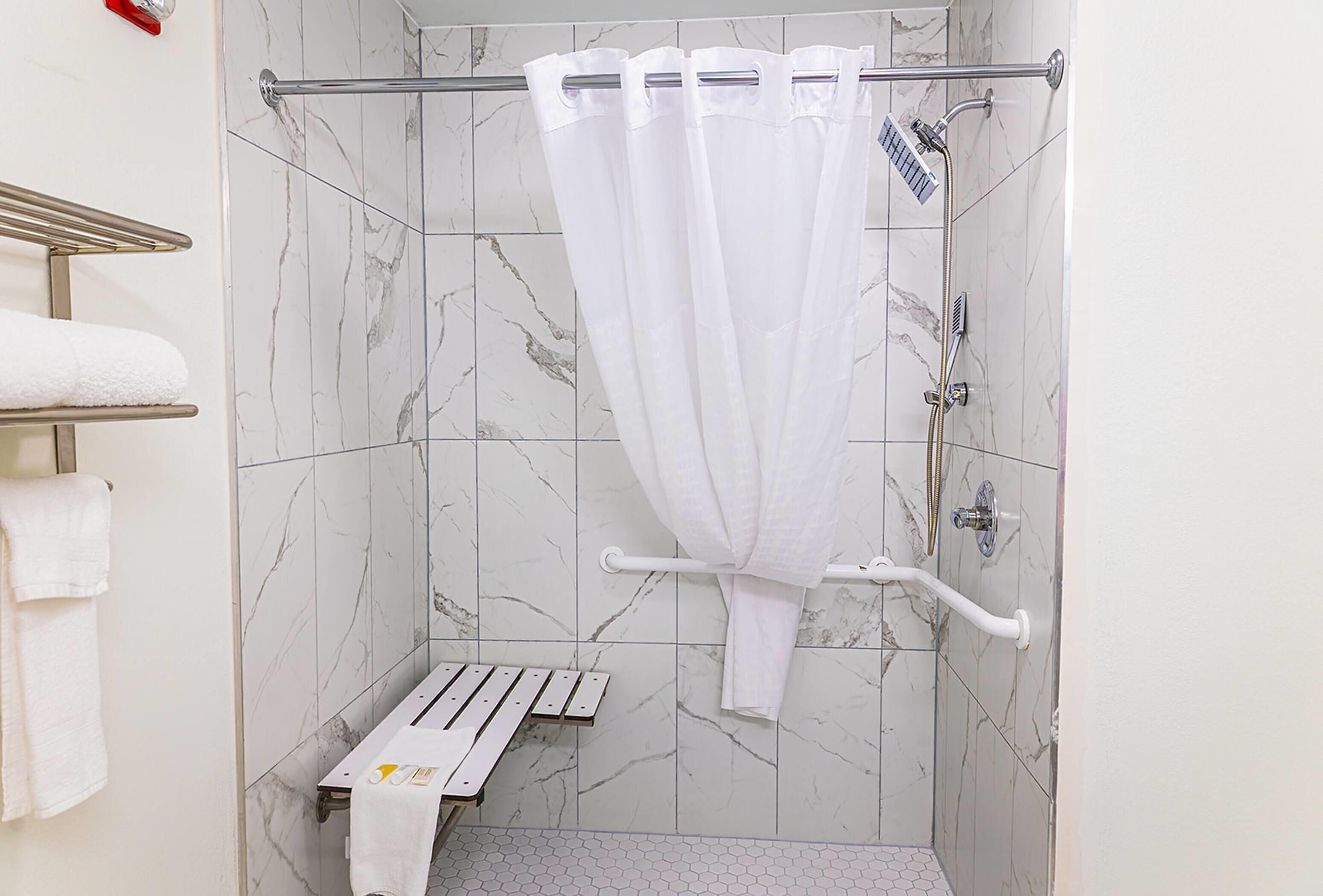 Ducha con cortina blanca, barra de apoyo y toallero con toallas.