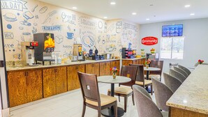 A breakfast bar with a coffee machine, seating area with chairs, and a wall decorated with food and coffee-related drawings. - Baymont by Wyndham Port Wentworth (Port Wentworth)
