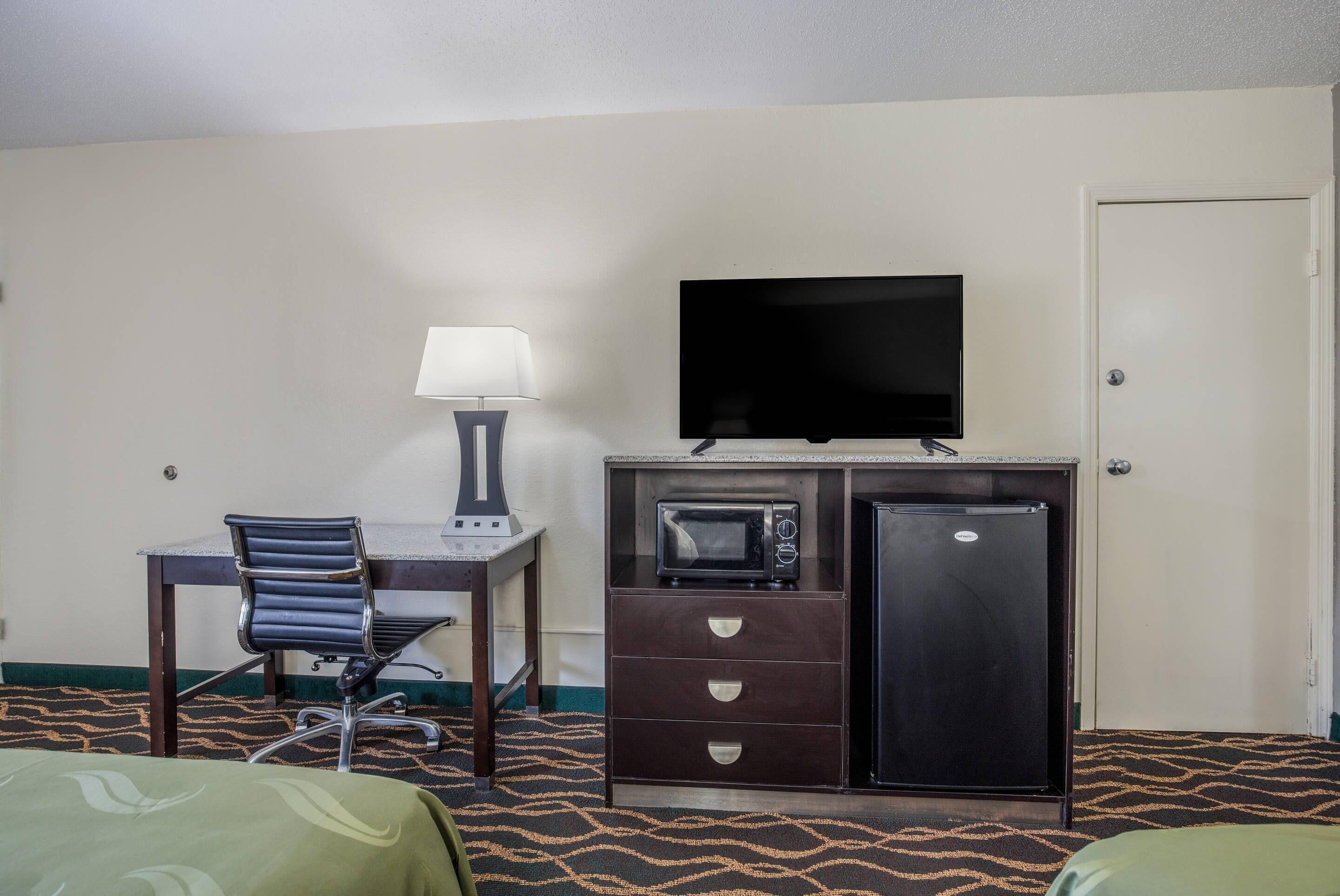 Habitación de hotel con cama, escritorio con silla, televisión, microondas y refrigerador.