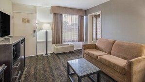 A hotel room with a sofa, a coffee table, a TV, a lamp, and a window with curtains. - Quality Inn & Suites Conference Center (Thomasville)