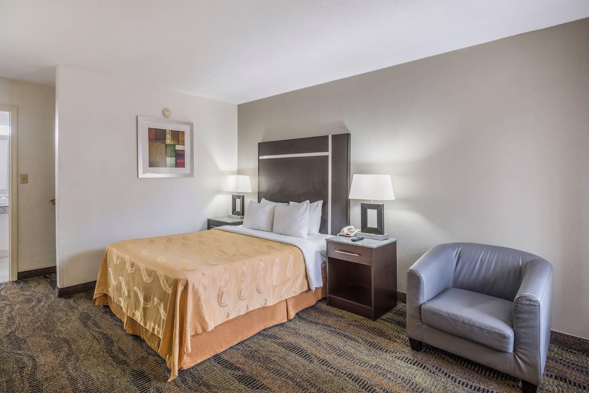 Une chambre d’hôtel avec un lit, deux tables de chevet avec des lampes, une chaise et un sol recouvert d’une moquette.