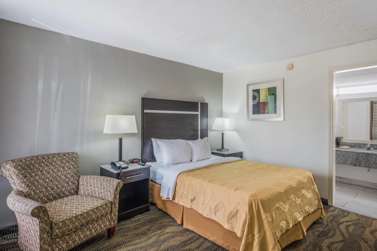 Une chambre d’hôtel avec un lit, deux lampes de chevet, une chaise, une table de chevet et un tableau au mur.