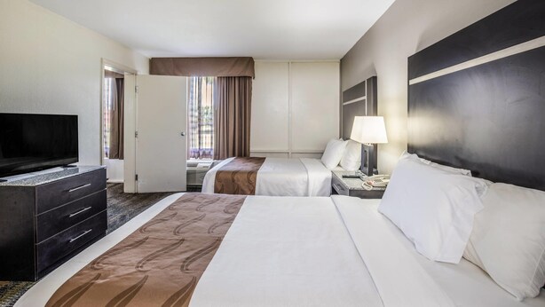 A hotel room with two beds, a television, a desk with a lamp, and a wardrobe. - Quality Inn & Suites Conference Center (Thomasville)