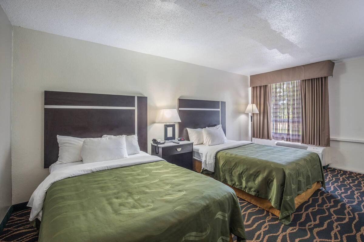 Une chambre d’hôtel avec deux lits, une table de chevet, une lampe et une fenêtre avec des rideaux.